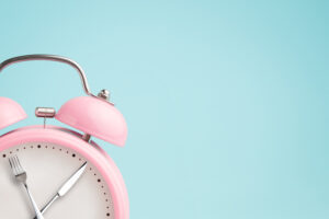 Pink alarm clock with fork and knife for hands for intermittent fasting | Reproductive Science Center of the SF Bay Area