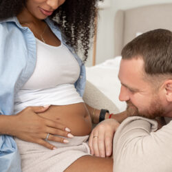 Smiling man looks at his wife's belly as they discuss their IVF options | Reproductive Science Center of the SF Bay Area